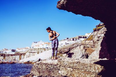 Rear view of woman exercising on rocky shore