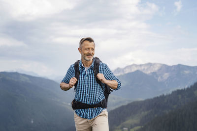 Full length of smiling man standing on mountain against sky