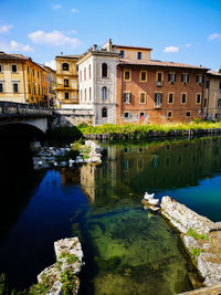 Bridge over canal by buildings against sky in city
