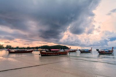 Boats moored on sea against cloudy sky during sunset