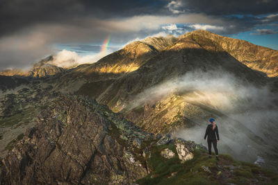 Rear view of man standing on mountain against sky