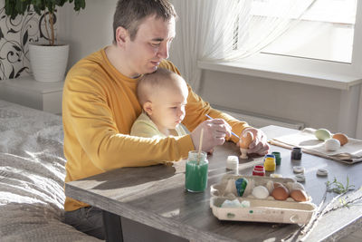 Dad with a child a little boy are preparing for easter, painting eggs, having lunch and having fun.