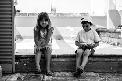 Full length portrait of siblings sitting outdoors