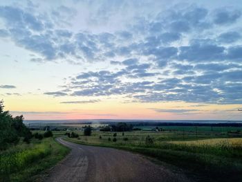 Road amidst field against sky during sunset