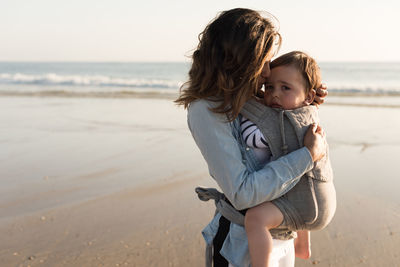 Mother carrying son while standing at beach