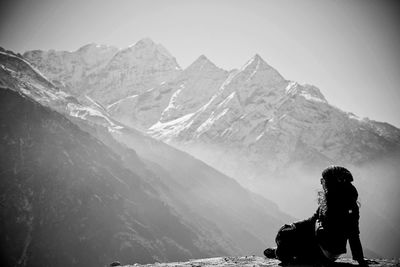 Woman sitting on rock by snowcapped mountains in foggy weather