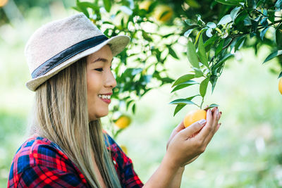 Smiling woman picking oranges in orchard
