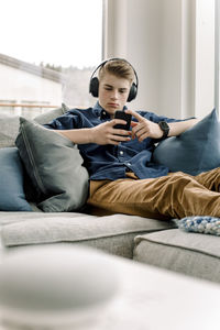 Teenage boy using smart phone while wearing headphones at home