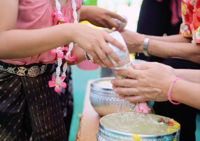 Midsection of woman pouring water on man hand