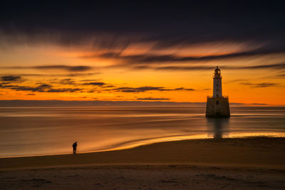 Silhouette tower on beach against sky during sunset