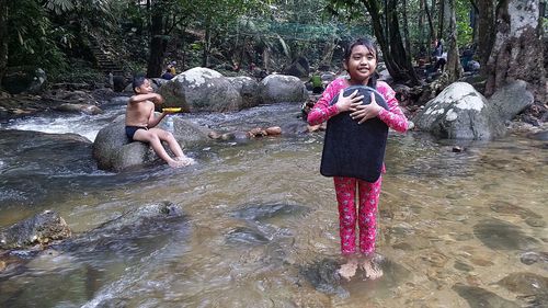 Portrait of happy girl standing on rock against trees