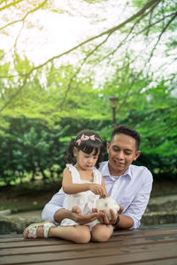 Father and daughter inserting coin in piggy bank