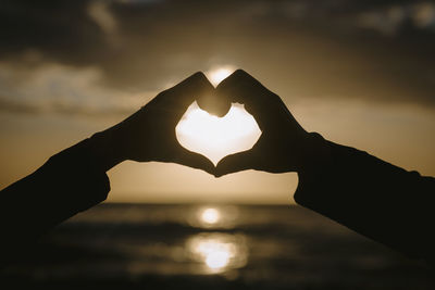 Heart shape on hand against sky during sunset