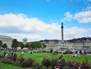 People relaxing at schlossplatz against cloudy blue sky