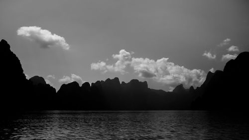 Scenic view of sea by silhouette mountain against sky