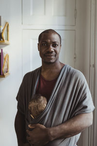 Portrait of man with baby boy in carrier at home