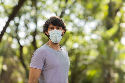 Handsome man wearing a medical protective mask on his face on a sunny day at park.