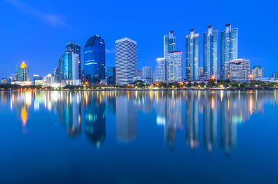 Reflection of illuminated buildings in city against blue sky