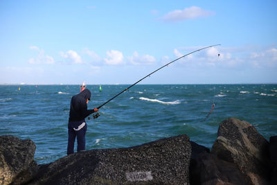 Rear view of man fishing in sea against sky