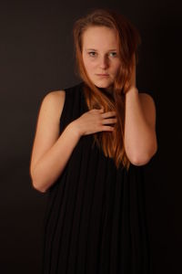 Portrait of beautiful young woman standing against black background