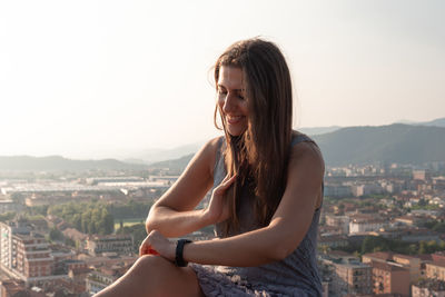 Beautiful woman smiling against buildings in city against sky