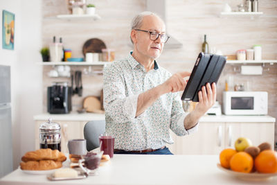 Senior man using digital tablet while standing at kitchen
