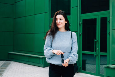 Portrait of young woman standing against wall