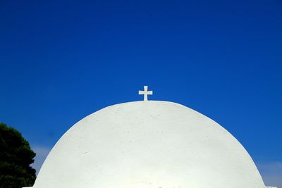 Low angle view of cross amidst buildings against clear blue sky