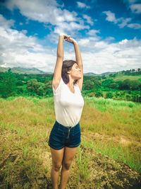 Full length of young woman standing on field against sky