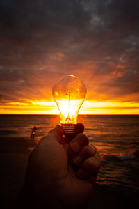 Person hand holding sea during sunset