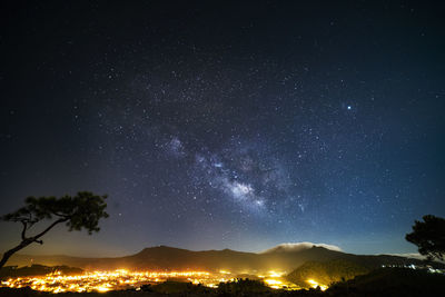 Low angle view of star field over illuminated city at night