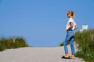 Woman standing on beach against clear blue sky