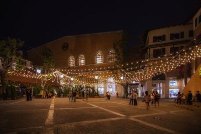 People at illuminated city against sky at night