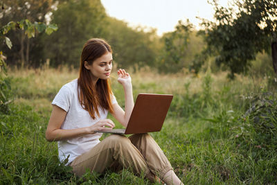 Young woman using laptop while sitting on field