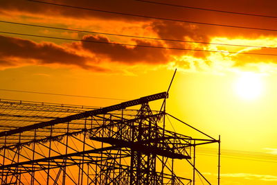 Low angle view of silhouette cables against orange sky