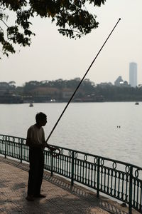 Rear view of man fishing on sea against clear sky