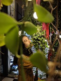 Young woman looking away seen through plants outdoors