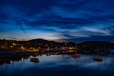 Sailboats moored in city against sky at dusk