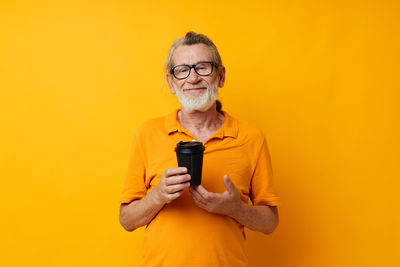 Portrait of young woman holding mobile phone against yellow background