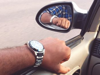 Close-up of man hand reflecting on side-view car mirror