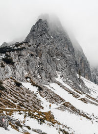 Tiny human walking on snow covered path under magnificent misty mountain