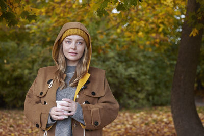 Portrait of young woman standing against trees