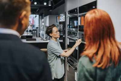 Side view of saleswoman assisting couple in buying microwave oven at electronics store