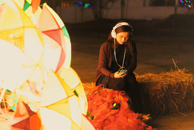 Woman in headphones sitting by illuminated lantern at night