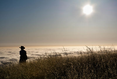 Silhouette person standing on grassy field against sky during sunset