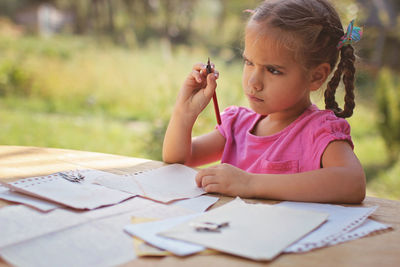 Cute girl looking away whole holding pencil outdoors