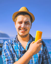 Portrait of young man holding camera against clear sky