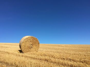 Hay bales on field against clear blue sky