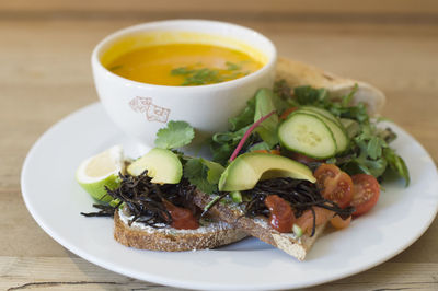 Yellow pumpkin soup with fresh herbs in a bowl with vegetables o a plate