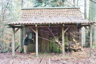 Man standing by abandoned house in forest
